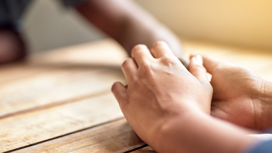 Two people touching each other's hands across a wooden table